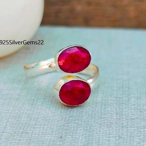 Könnte beinhalten: Ein silberner Ring mit zwei roten Edelsteinen. Der Ring ist so konzipiert, dass er sich um den Finger wickelt.