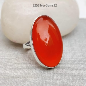 May include: A silver ring featuring a large, oval-shaped, bright orange carnelian gemstone. The ring is set in a simple, silver band.