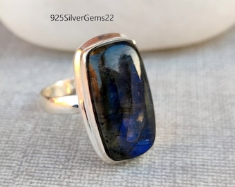 Può includere: Un anello d'argento con una pietra preziosa in labradorite blu scuro. La pietra è rettangolare e ha una finitura scintillante e iridescente.