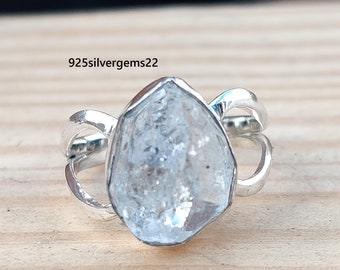 May include: A silver ring with a clear, faceted, rough-cut gemstone. The ring has a simple, modern design with a twisted band.