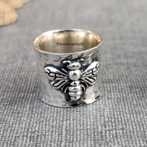 May include: A silver ring with a hammered texture and a bee design. The ring is engraved with the text "925silvergems22".