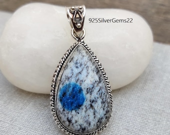 Puede incluir: Un colgante de plata con una piedra preciosa de cianita azul y blanca. El colgante tiene forma de lágrima y tiene un borde de plata detallado.