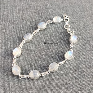 Könnte beinhalten: Ein silbernes Kettenarmband mit ovalen Mondsteinperlen. Das Armband hat einen Karabinerverschluss.