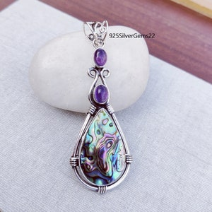 May include: A silver pendant with a teardrop-shaped abalone shell inlay and two amethyst gemstones. The pendant has a silver bail for attaching to a chain.