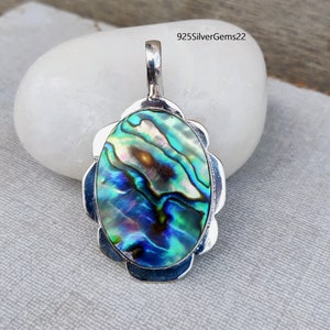 Könnte beinhalten: Ein silberner Anhänger mit einem ovalen Einlegeteil aus Abalone-Muschel. Die Muschel hat schillernde blaue, grüne und violette Farben.