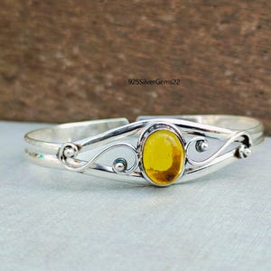 Op de afbeelding: Een zilveren armband met een gele ovale edelsteen gezet in een delicaat swirl-ontwerp. 925SilverGems22 is afgedrukt op de afbeelding.