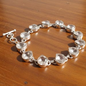 Peut inclure: Un bracelet en argent orné de pierres précieuses claires et facettées. Le bracelet est doté d'un fermoir à bascule et est composé de plusieurs pierres serties en lunette, reliées entre elles. Les pierres sont ovales et rondes.