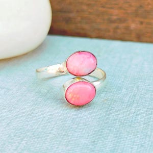 May include: A silver ring with two pink oval-shaped stones. The stones are set in a silver band that wraps around the finger.