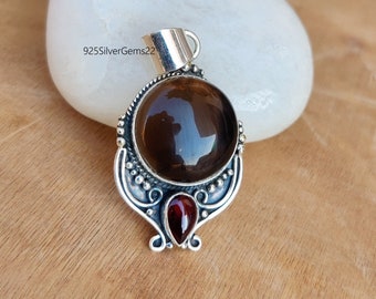 May include: A silver pendant with a brown gemstone and a red gemstone. The pendant has a detailed design with a swirl pattern.