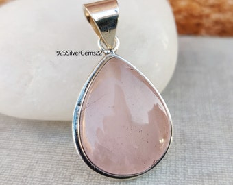 Puede incluir: Un colgante en forma de lágrima con una piedra de cuarzo rosa rosa claro engastada en un engaste de plata de ley. El colgante está sobre un fondo blanco.