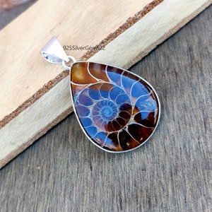 May include: A silver pendant featuring a brown and blue ammonite fossil. The pendant is in the shape of a teardrop and has a silver bail.