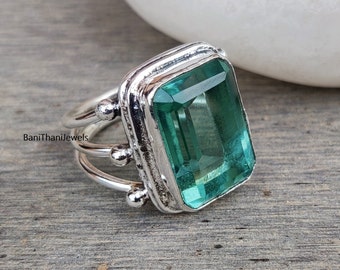 May include: A silver ring with a large, emerald green gemstone set in a square bezel. The ring has a triple band design with small beads on the sides.