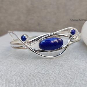 May include: A silver bracelet featuring a blue lapis lazuli stone and two smaller blue stones. The bracelet has a delicate, intricate design.
