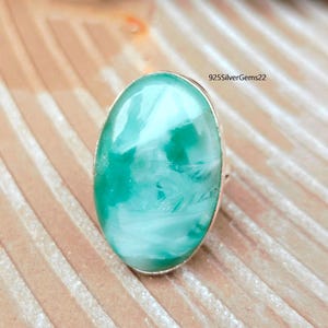 May include: Oval-shaped ring featuring a large, polished gemstone with a marbled turquoise and white pattern. The gemstone is set in a silver-colored metal band. The text "925SilverGems22" is visible on the upper right side of the image.