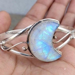 Op de afbeelding: Een zilveren manchetarmband met een maanvormige maansteen. De maansteen heeft een blauw-witte iriserende gloed. De armband heeft een delicaat, open ontwerp met decoratieve krullen en kleine zilveren kralen. De tekst "925SilverGems22" is zichtbaar.