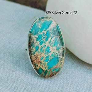 May include: A silver ring with a large oval turquoise and gold jasper gemstone. The stone has a swirling pattern of blue, green, and gold.