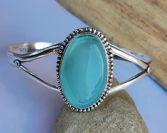 May include: A silver bangle bracelet with a light blue oval gemstone set in a beaded bezel. The bracelet has a delicate, openwork design.