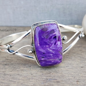 Pode incluir: Um bracelete de prata com uma pedra grande, retangular, de cor púrpura e branca no centro. A pedra tem um padrão de redemoinho.