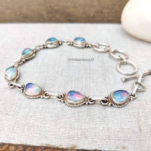 May include: A silver bracelet with a toggle clasp features iridescent oval-shaped stones. The bracelet is made of sterling silver and has a delicate chain design.