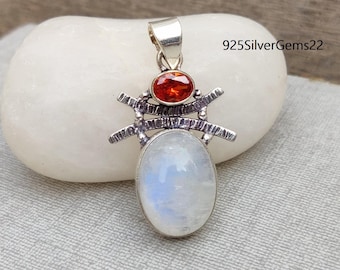May include: Silver pendant featuring a white moonstone and a red gemstone. The pendant is in the shape of a spider with a detailed design.