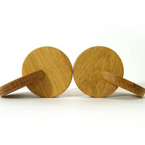 May include: Two wooden round knobs with a handle on each side. The knobs are light brown and have a natural wood grain.