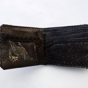 May include: A black leather wallet with a textured surface and a clear plastic window for an ID card.