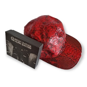 May include: A red snakeskin baseball cap with a black box that says "Rifoy Leather Reptile Specialist".