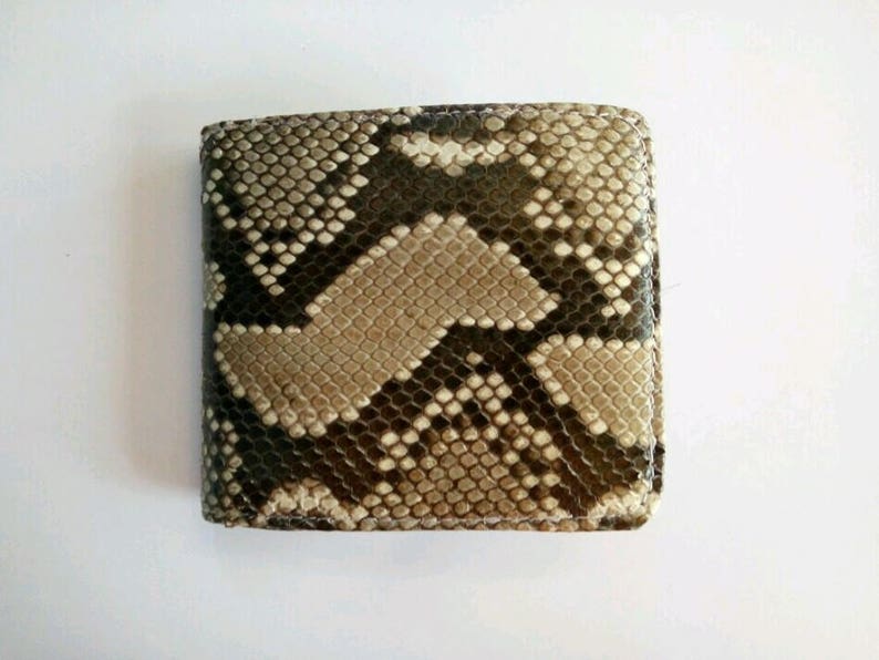 May include: A square bi-fold wallet with a snakeskin pattern. The wallet features a mix of brown, tan, and black scales. The texture of the wallet is visible, and the edges are neatly stitched.