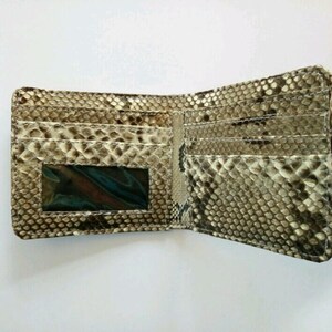 May include: Open, textured wallet with a snakeskin pattern in shades of brown, tan, and cream. The wallet is open, revealing multiple card slots and a clear ID window. The interior is a lighter shade of tan.