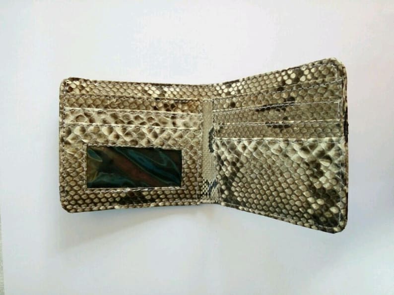 May include: Open, textured wallet with a snakeskin pattern in shades of brown, tan, and cream. The wallet is open, revealing multiple card slots and a clear ID window. The interior is a lighter shade of tan.