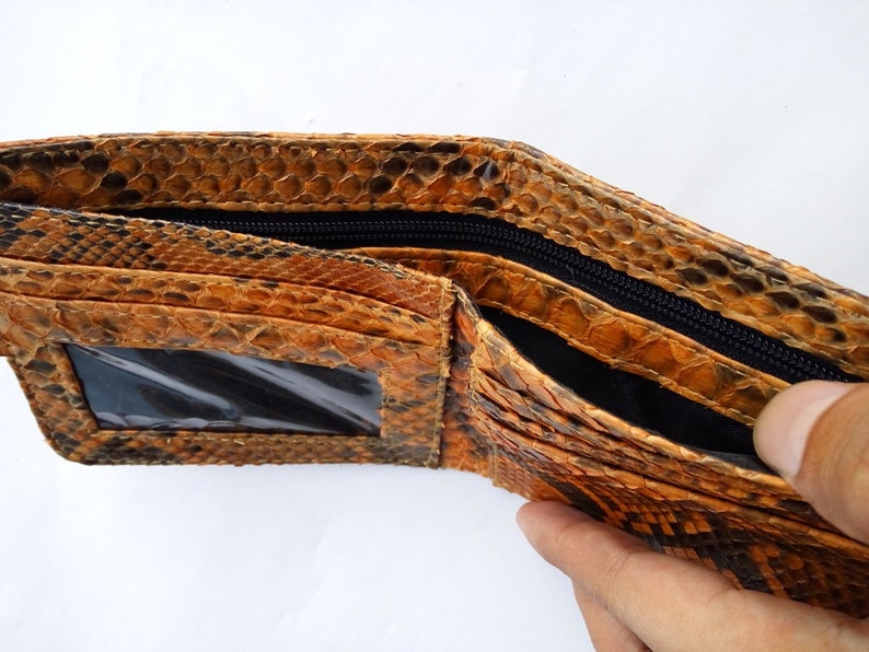May include: A brown and black snakeskin wallet with a zippered closure and a clear plastic window for identification.