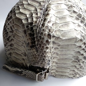 May include: A grey snakeskin cap with a silver buckle closure. The cap is made of genuine snakeskin and has a unique texture.