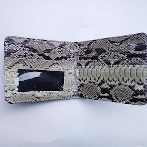 May include: A light brown snakeskin wallet with a clear plastic ID window. The wallet is open and the inside is lined with a black fabric.