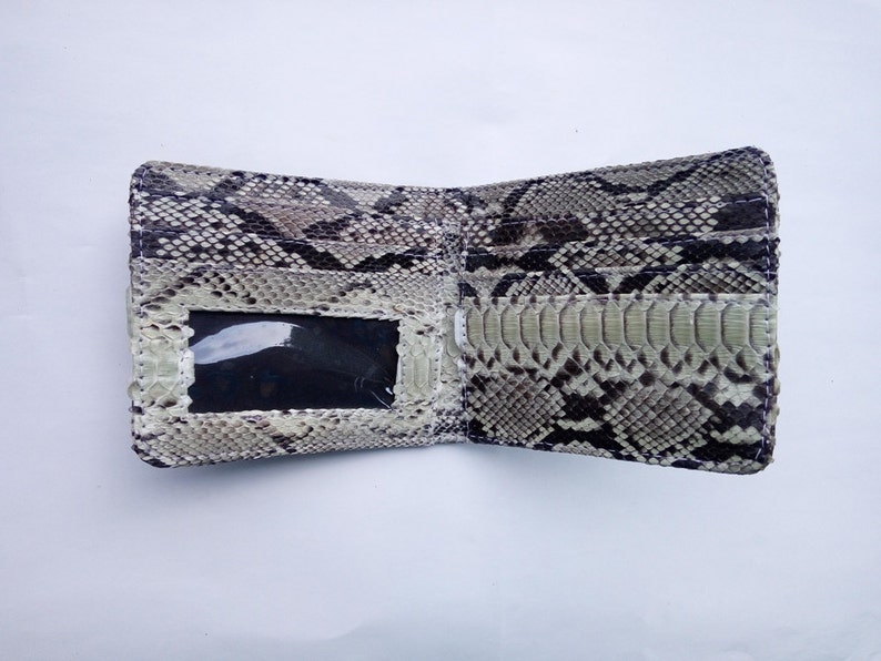 May include: A light brown snakeskin wallet with a clear plastic ID window. The wallet is open and the inside is lined with a black fabric.