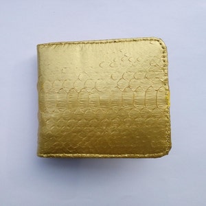 May include: A bi-fold wallet in a metallic gold finish with a textured snakeskin pattern. The wallet features visible stitching along the edges and a rectangular shape with rounded corners on the right side, showcasing a consistent gold tone.