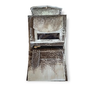 May include: A bi-fold wallet with a reptile skin pattern in shades of gray and white. The wallet has multiple compartments, including a clear ID window and a zippered pocket. The top flap folds over and secures with a snap closure.