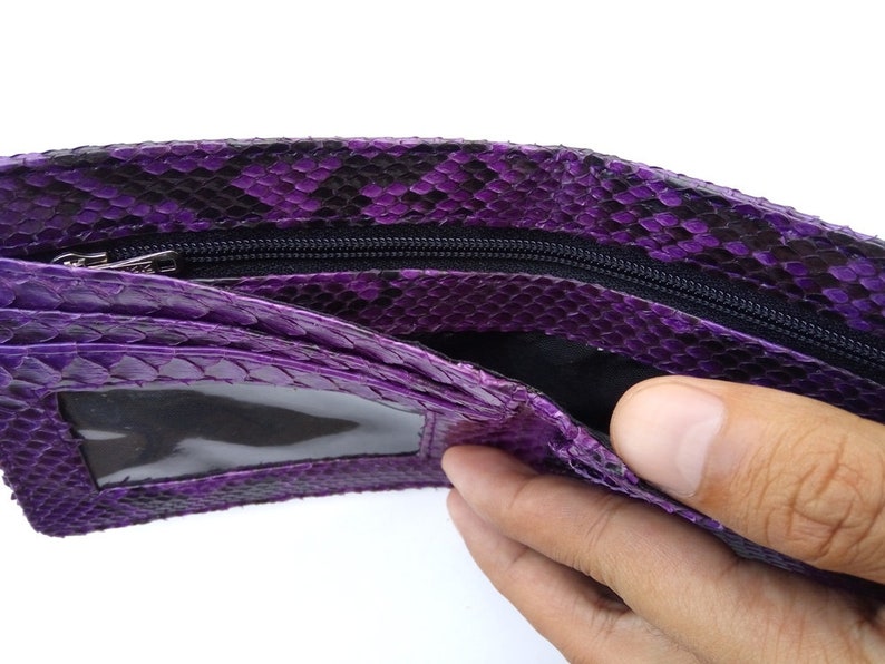May include: Purple snakeskin wallet with a zipper closure and a clear plastic window. The wallet is open and a hand is reaching inside.