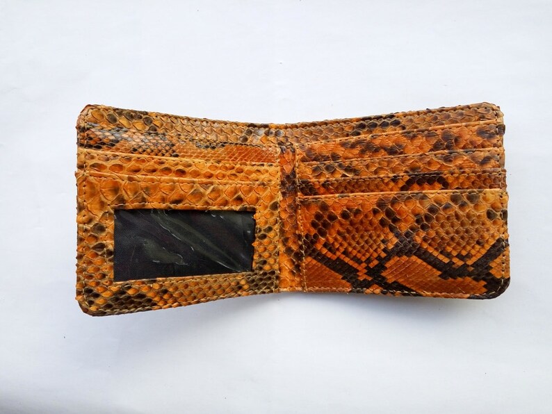 May include: A brown and orange snakeskin wallet with a clear plastic window for an ID card. The wallet is open and has multiple card slots.