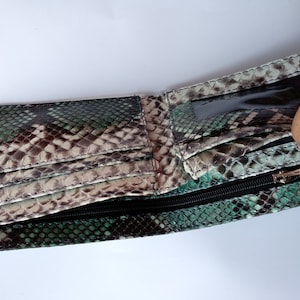 Op de afbeelding: Een groene en bruine slangenleren portemonnee met een ritssluiting en een transparant plastic ID-venster.