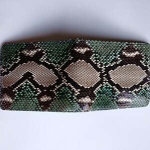 Op de afbeelding: Een groene, bruine en witte slangenleren portemonnee. De portemonnee is dichtgevouwen en heeft een glad, getextureerd oppervlak.