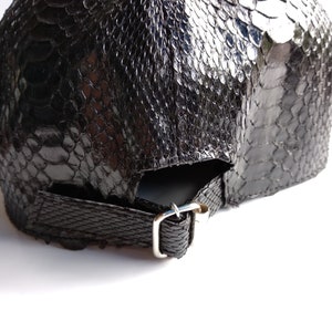 May include: Black leather baseball cap with a snakeskin pattern. The cap has an adjustable strap with a metal buckle.