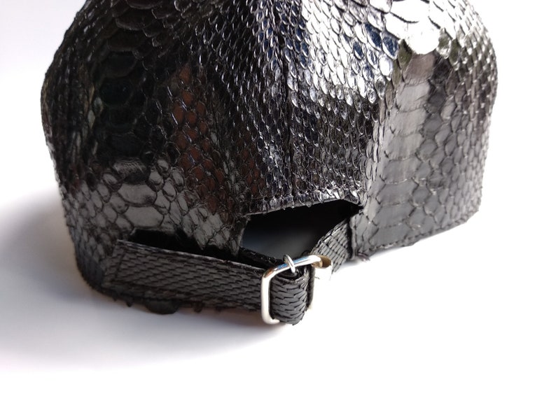 May include: Black leather baseball cap with a snakeskin pattern. The cap has an adjustable strap with a metal buckle.