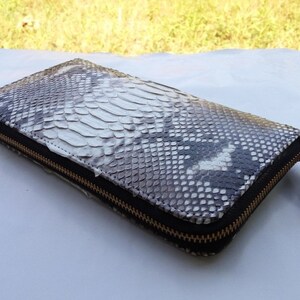 May include: A long, black and white snakeskin wallet with a gold zipper.
