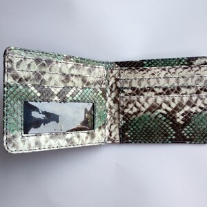 Op de afbeelding: Een portemonnee met twee vouwen gemaakt van groene en bruine slangenleer met een transparant plastic venster aan de voorkant.