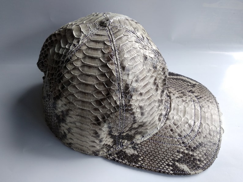 May include: A grey snakeskin baseball cap with a curved brim. The cap is made of genuine snakeskin and has a unique, textured pattern.