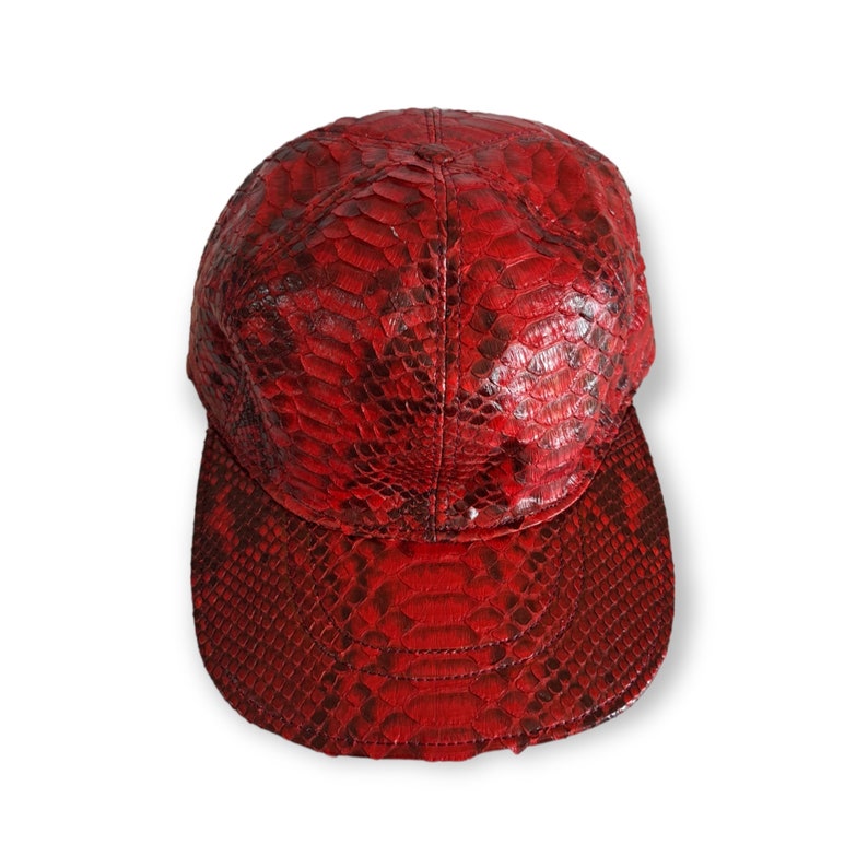 May include: A red snakeskin baseball cap with a curved brim. The cap is made of genuine leather and has a snakeskin pattern.