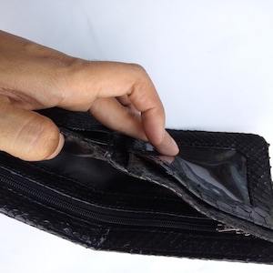May include: Black leather wallet with a zipper closure and a clear plastic window. The wallet is made of snakeskin.