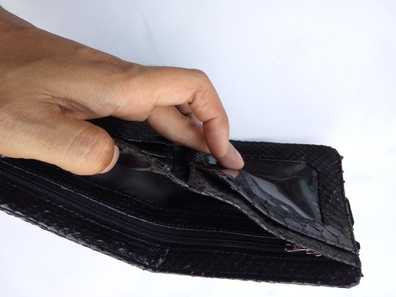 May include: Black leather wallet with a zipper closure and a clear plastic window. The wallet is made of snakeskin.