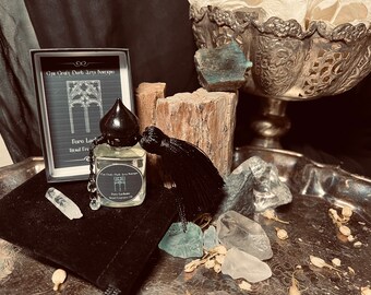 Può includere: Una bottiglia nera con un tappo nero e un fiocco, contenente un liquido trasparente. La bottiglia è etichettata "Pure Incense" e "Burnt Tree" e si trova su un vassoio d'argento con cristalli e una piccola borsa di velluto nero. La bottiglia è anche etichettata "Cry Craft Dark Arts Boutique".