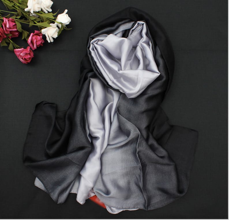 May include: A black and silver gradient silk scarf. The scarf is folded and draped on a black surface.